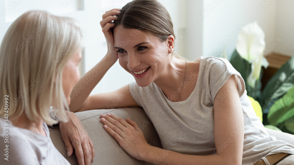 Smiling grownup millennial girl sit on couch have fun talking enjoying weekend with middle-aged mother, happy senior mom and adult daughter relax on sofa chatting, sharing secrets or gossiping Smiling grownup millennial girl sit on couch have fun talking enjoying weekend with middle-aged mother, happy senior mom and adult daughter relax on sofa chatting, sharing secrets or gossiping