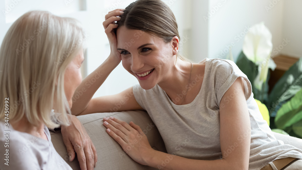 Smiling grownup millennial girl sit on couch have fun talking enjoying weekend with middle-aged mother, happy senior mom and adult daughter relax on sofa chatting, sharing secrets or gossiping