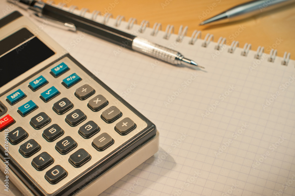 an old calculator black glasses a notepad a pencil on a yellow wooden board an old calculator black glasses a notepad a pencil on a yellow wooden board