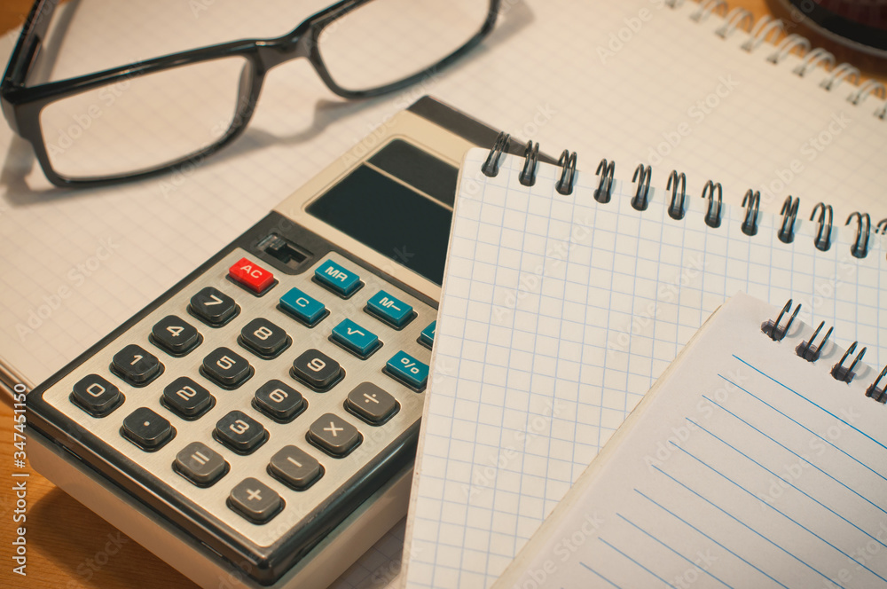 an old calculator black glasses a notepad on a yellow wooden board an old calculator black glasses a notepad on a yellow wooden board