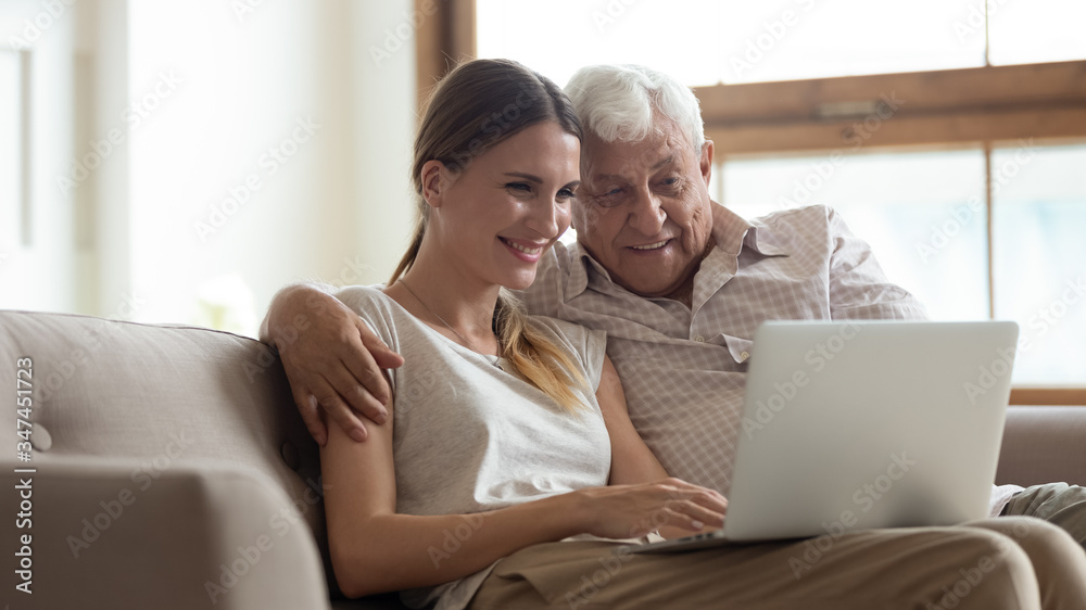 Smiling mature 80s dad sit rest on sofa in living room with grownup daughter using modern computer together, happy senior father and adult millennial girl relax on couch at home browsing on laptop Smiling mature 80s dad sit rest on sofa in living room with grownup daughter using modern computer together, happy senior father and adult millennial girl relax on couch at home browsing on laptop