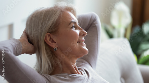 Close up of happy mature woman sit relax on sofa in living room breathing fresh air, smiling calm middle-aged female rest on couch at home daydreaming or enjoying leisure weekend, stress free concept © fizkes