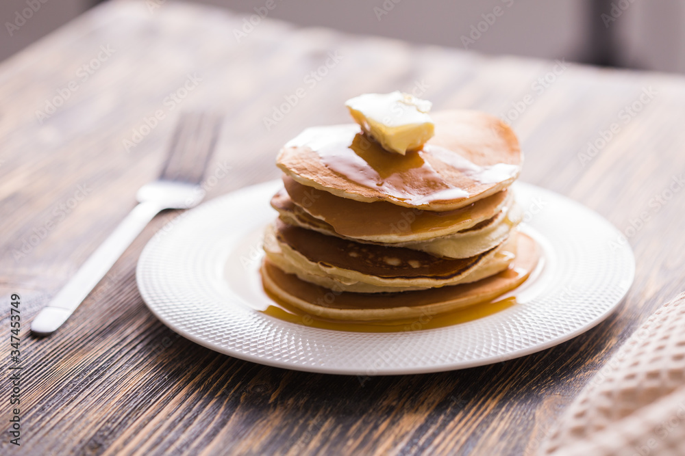 Small pancakes with maple syrup and butter on wooden table. Breakfast concept.