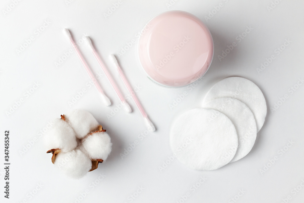 Fototapeta premium Cosmetics and self-care. On a white background, cotton pads, cotton sticks, a cotton flower and a jar of cream are beautifully laid out. Flat lay