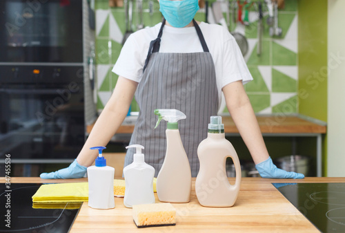 Woman in mask and gloves showing all eco detergents for kitchen disinfection
