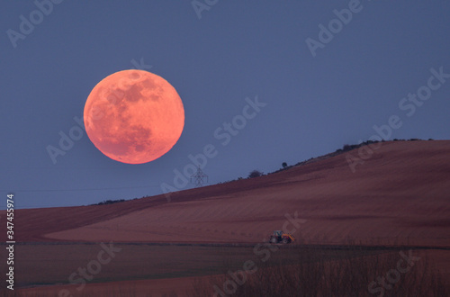 luna roja en el horizonte con tractor agricola