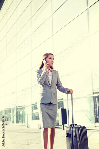 Portrait of young attractive businesswoman talking on smartphone with her suitcase in airport
