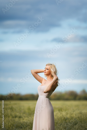 Woman stands in the middle of a green field and a blue sky with clouds