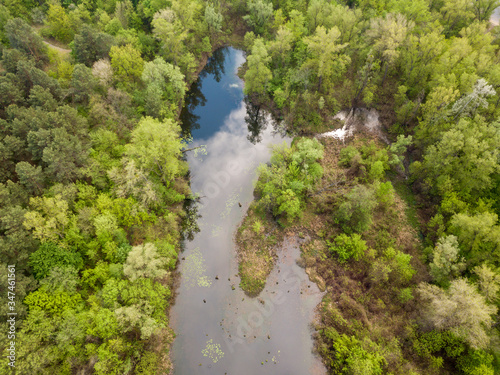 A small lake in a deciduous forest. Clouds are reflected in the water. Aerial drone view.