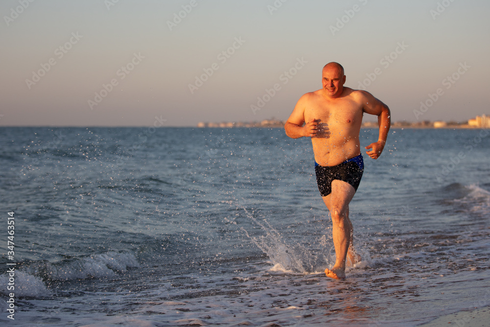 An elderly man jogs along the coast.