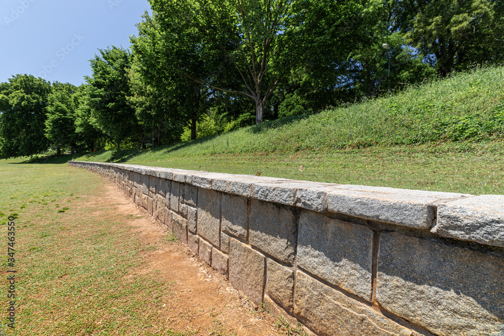 Long low retaining wall along a hillside in a public park, green grass and trees, horizontal aspect Long low retaining wall along a hillside in a public park, green grass and trees, horizontal aspect