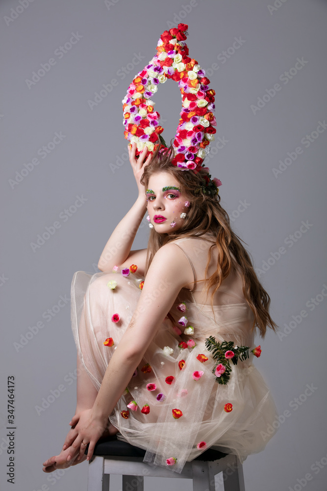 Beautiful girl in a fabulous look with flower horns sits on a chair. Maleficent. Spring or summer beauty. Woman in the image of a flower.