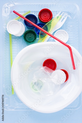 Pile of single use plastic garbage including water bottles, drinking straws, plate, fork, knief and bottle caps in box for food