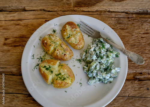 Baked potatoes with cheese and cocumber salad with sour cream on white plate.