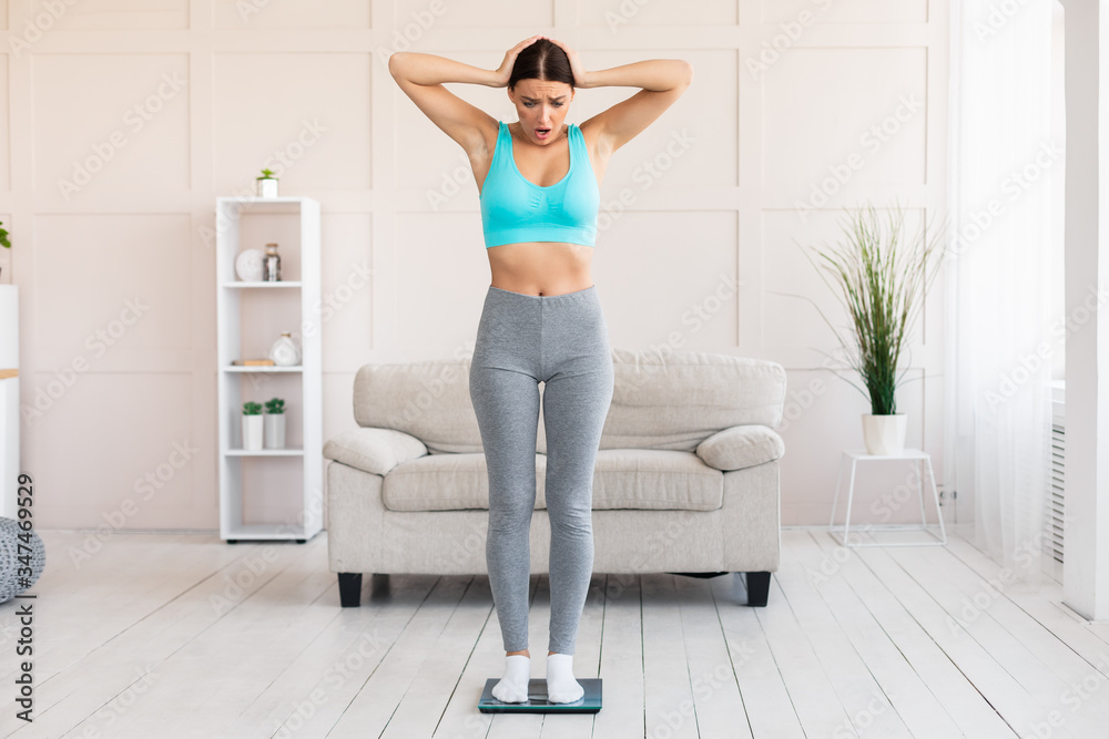 Fototapeta premium Shocked Woman Standing On Weight Scales Gaining Kilograms At Home