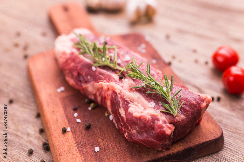 Fresh raw meat for steak on wooden cutting board, close-up.