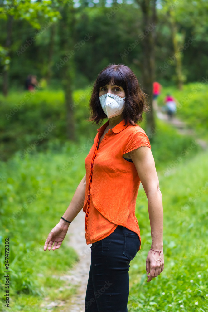 A young Caucasian woman in protective mask walking along a path. Covid-19 pandemic, social distance