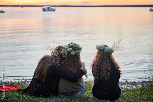 Three girls with wreaths of wild flowers by the lake. An evening at Saint John's Eve by the lake.
