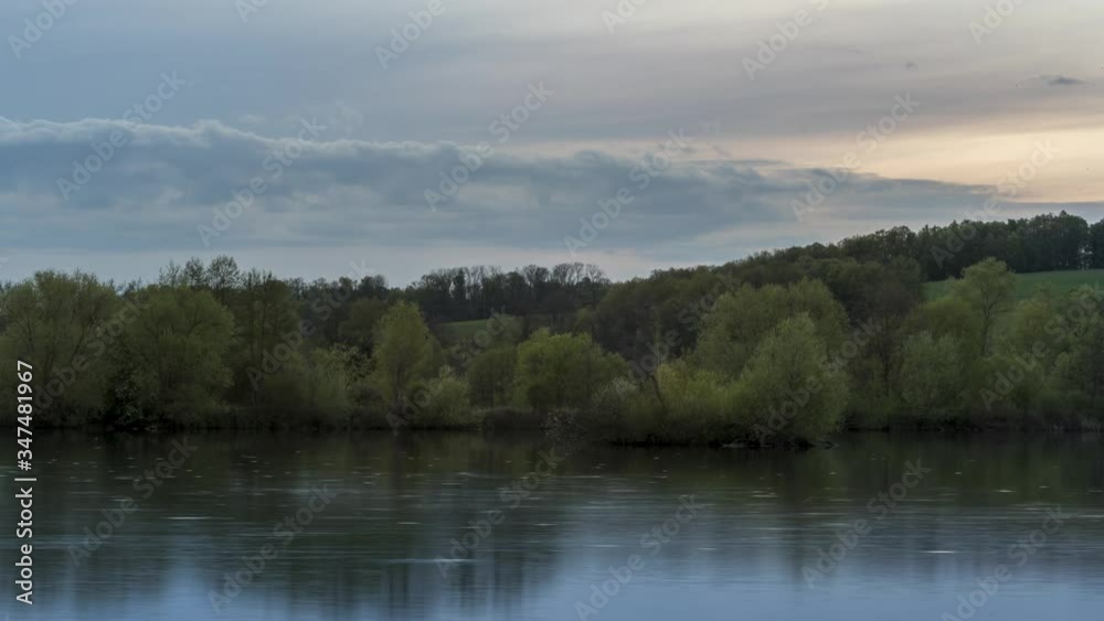 Timelapse of lake surface surrounded by trees with reflection of clouds that move in sky during the early evening summer time, clouds move and fish jump on the water surface Hustopece Czech Republic Timelapse of lake surface surrounded by trees with reflection of clouds that move in sky during the early evening summer time, clouds move and fish jump on the water surface Hustopece Czech Republic