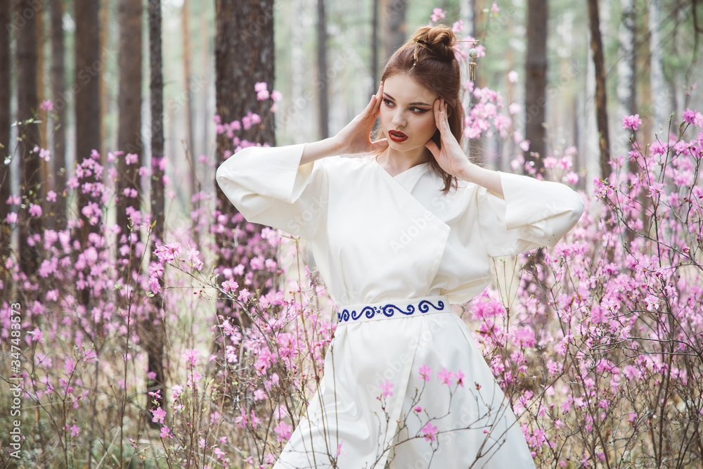 A girl dressed in Japanese style in a flowering forest among pink flowers A girl dressed in Japanese style in a flowering forest among pink flowers
