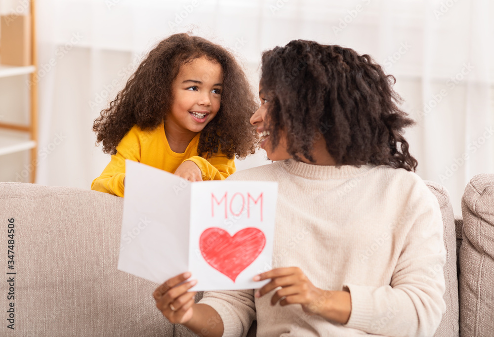 Little Black Girl Congratulating Happy Mother Sitting On Sofa Indoors Little Black Girl Congratulating Happy Mother Sitting On Sofa Indoors