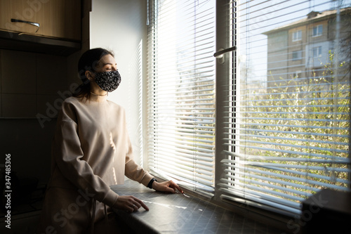 woman girl in a handmade black protective mask, stands at home near the window