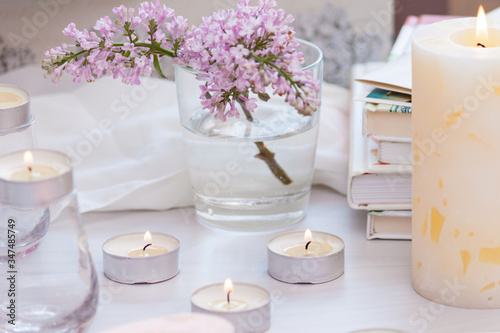 Pastel room interior decor with burning hand-made candle, books, flowers. Cozy and relax concept.