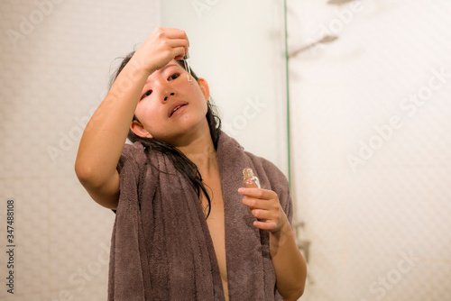 young beautiful and happy Asian Korean woman applying serum facial skin care and face treatment in the bathroom enjoying morning routine in beauty concept