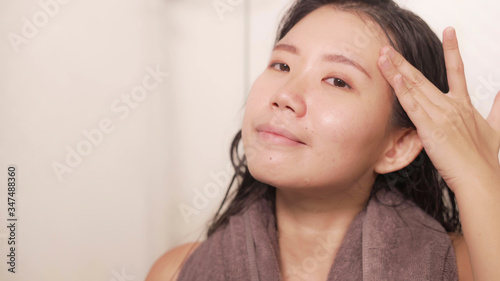 young happy and beautiful Asian Chinese woman applying moisturizer facial cream and beauty treatment at home bathroom in morning routine smiling cheerful and fresh