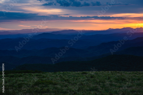 Sun Sets Behind Mountain Layers and Grassy Field © kellyvandellen