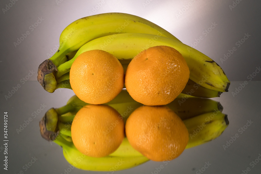Yellow bananas and oranges on mirroring table. Gorizontal image