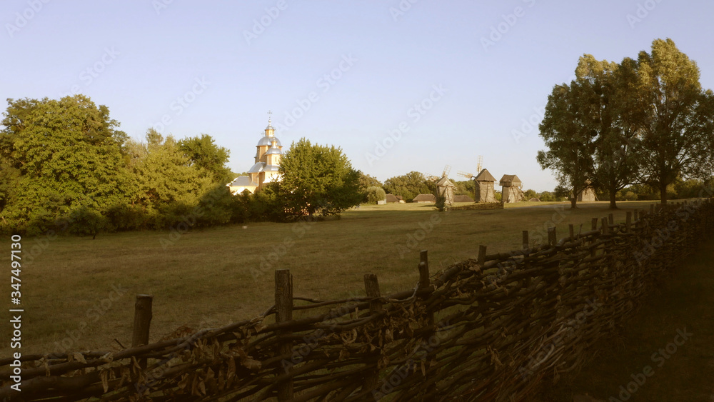 Large meadow is surrounded by wattle fence. Church and mills in the distance. Large meadow is surrounded by wattle fence. Church and mills in the distance.