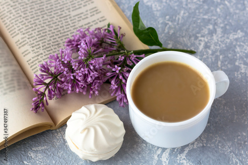 Coffee with milk and marshmallows. Reading a book in the garden with a cup of coffee. Romantic still life with lilac flowers.