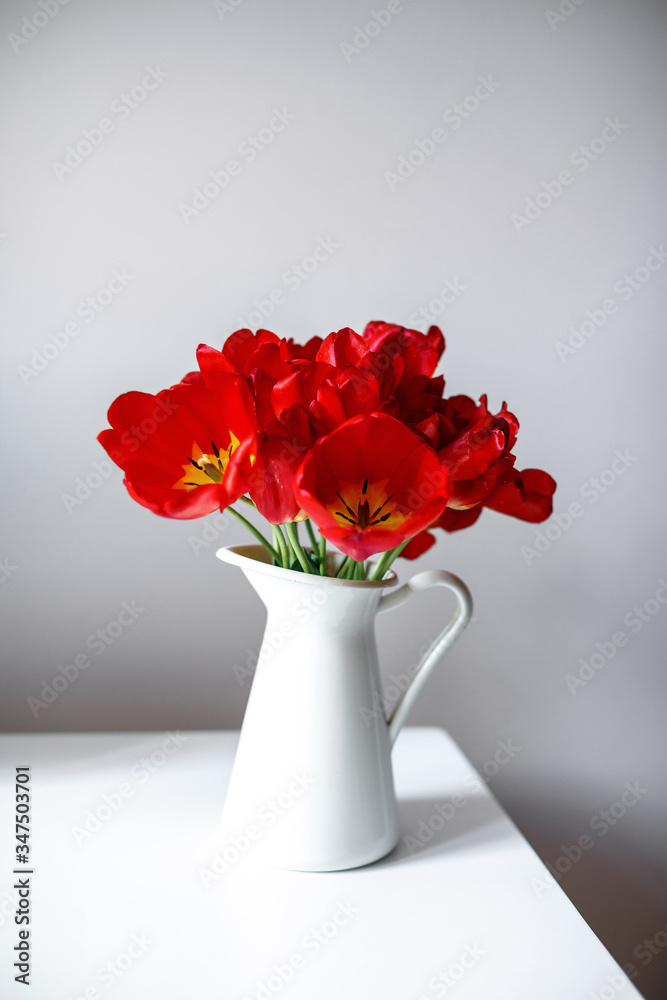 A beautiful bouquet of red tulips is standing in a white jug on the table. Festive bouquet as a gift. Focus on flowers. The concept of surprise.