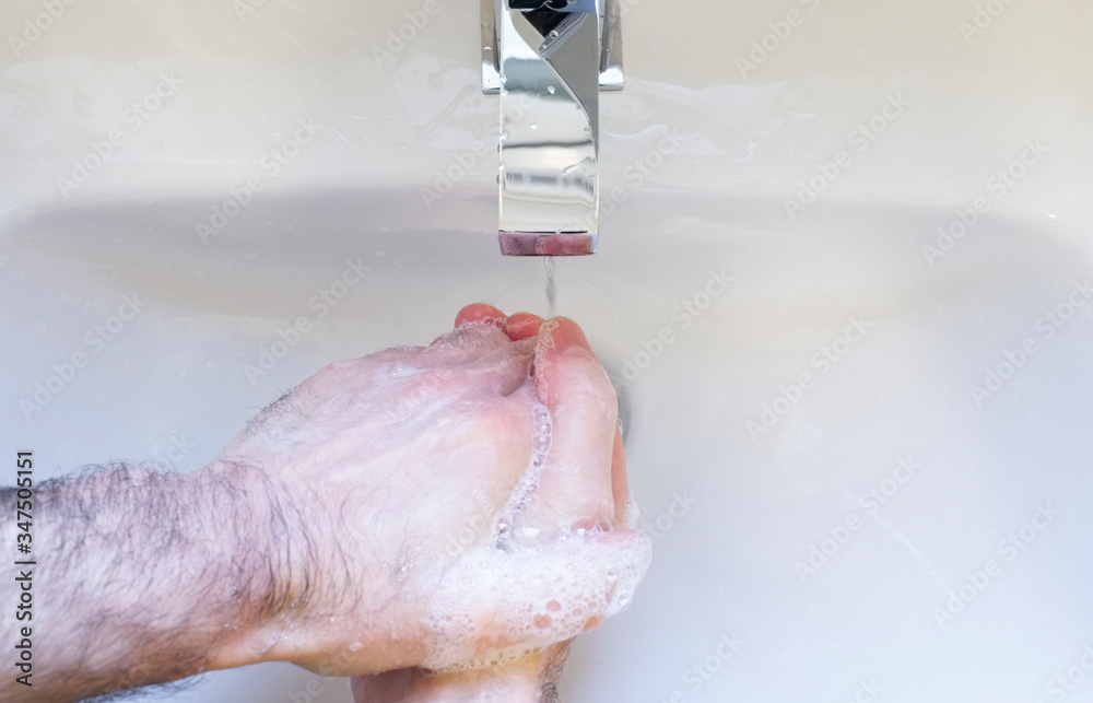 Fototapeta premium Soapy wet hands washing with blue anti-bacterial soap under tap