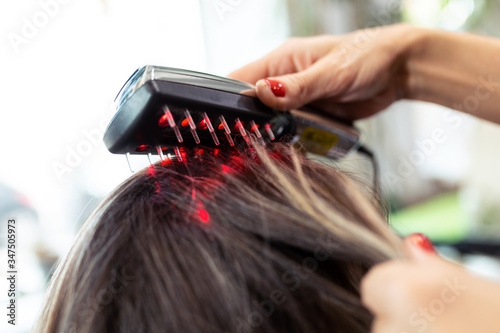 фотографія Hairdresser doing a treatment with ultrasonic and infrared laser comb for hair regrowth in her woman client at the salon