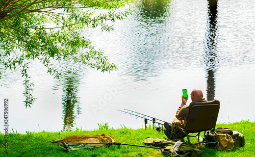 A fisherman catches fish on the river on a warm spring day. A fisherman is talking on the smartphone while fishing.Smartphone with green screen