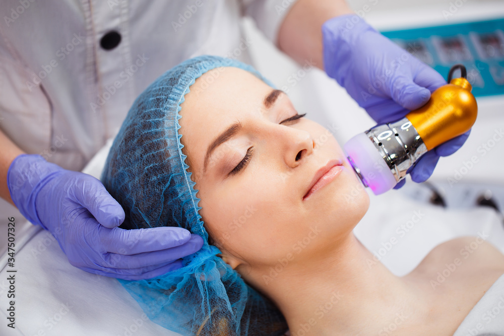 Fototapeta premium The procedure of photoepilation in the beauty salon. A young woman is removed unwanted hair on her face. Hardware cosmetology. Close up
