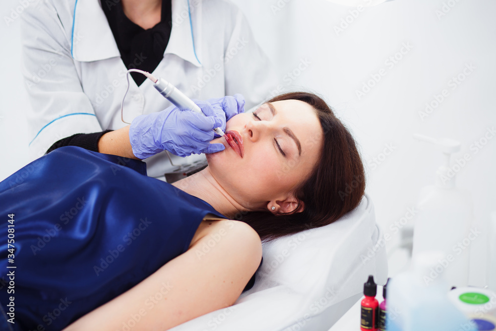 Young woman having permanent makeup on lips in beautician salon on a white background. Close up Young woman having permanent makeup on lips in beautician salon on a white background. Close up