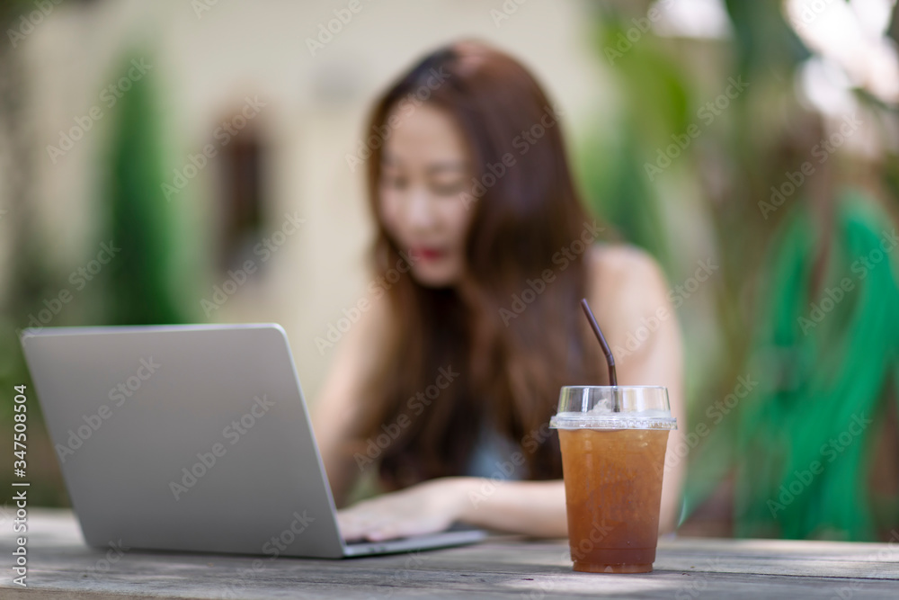 Iced lemon tea on the table Blur the background of a woman using a laptop Iced lemon tea on the table Blur the background of a woman using a laptop