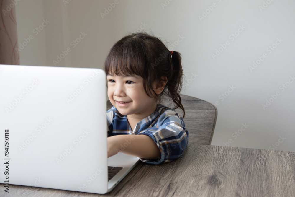 Adorable three-year-old Asian girl is training, learning and practicing to use a laptop happily and at home for education to grow up in the technology and digital world.