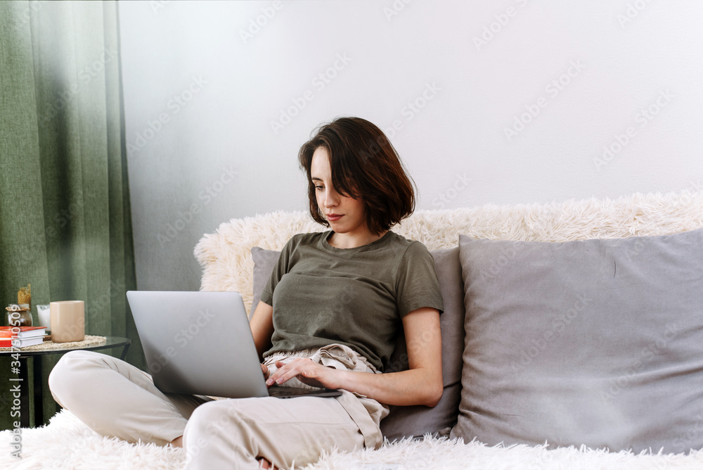 Young female using laptop, communicates on internet with customer in home on sofa. Cozy home office workplace, remote work, E learning concept on quarantine and self-isolation Young female using laptop, communicates on internet with customer in home on sofa. Cozy home office workplace, remote work, E learning concept on quarantine and self-isolation