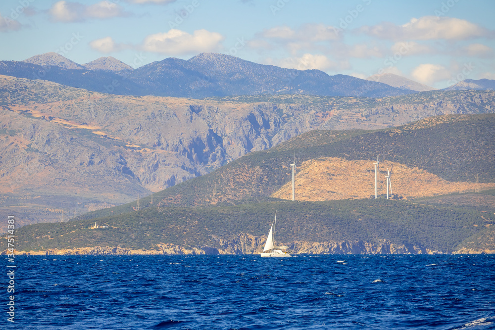 Sailing Yacht and Hilly Coast With Wind Farms