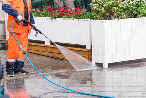 Worker washes the sidewalk in front of a street cafe - surface sanitation