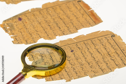 Book pages with an Arabic manuscript on a table with a light and a magnifying glass. Paleography, the study of ancient Arabic writing