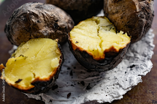 Baked in the fire potatoes in the skin according to the village recipe and method, directly in the ashes. Charred, fragrant tubers, a hot dish on a white stone plate