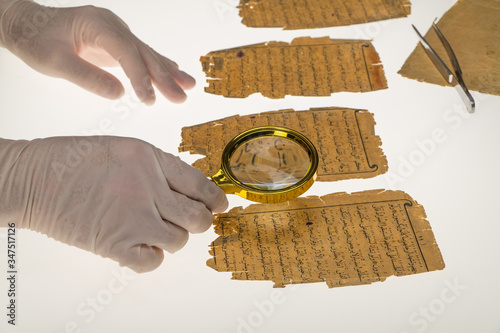 A researcher studies Arabic writing from the Koran using a magnifying glass and a table with a light. Paleography, the study of ancient Arabic writing