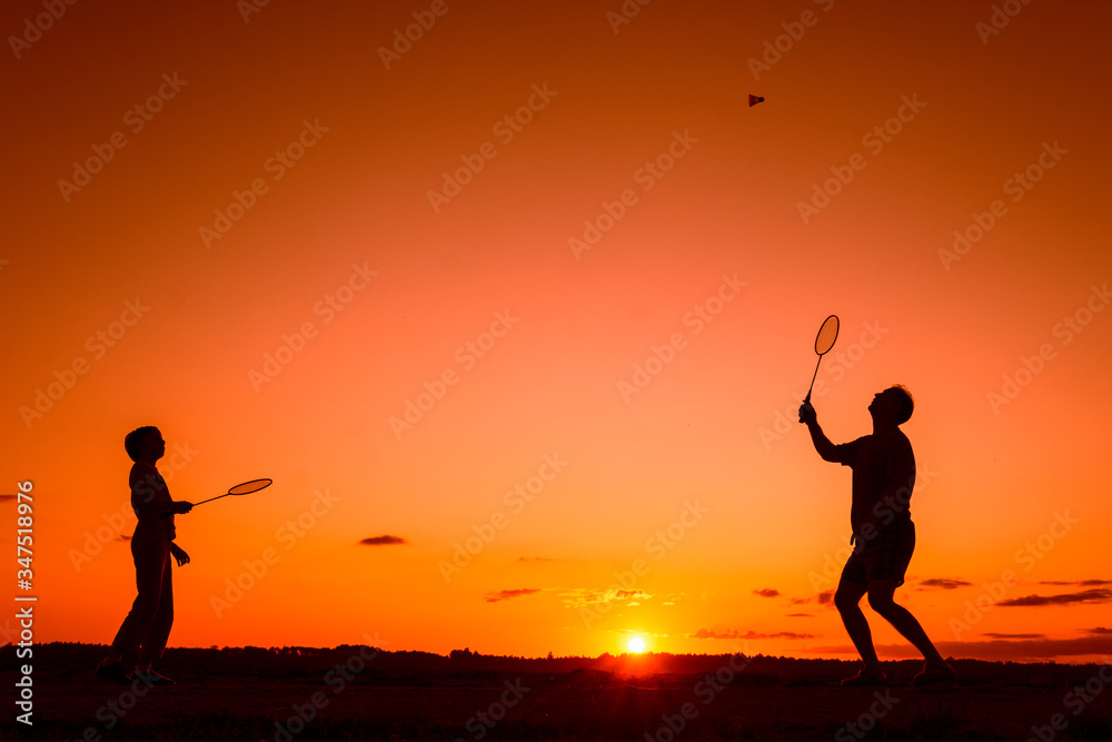 Father and son playing badminton in the evening, silhouettes of people exercising in nature, recreation, sport, lifestyle concept  