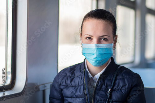 Young serious woman wearing medical protective mask on her face against coronavirus, beautiful girl sitting alone in train, public transport. Corona virus, pandemic, Covid-19, health, travel concept