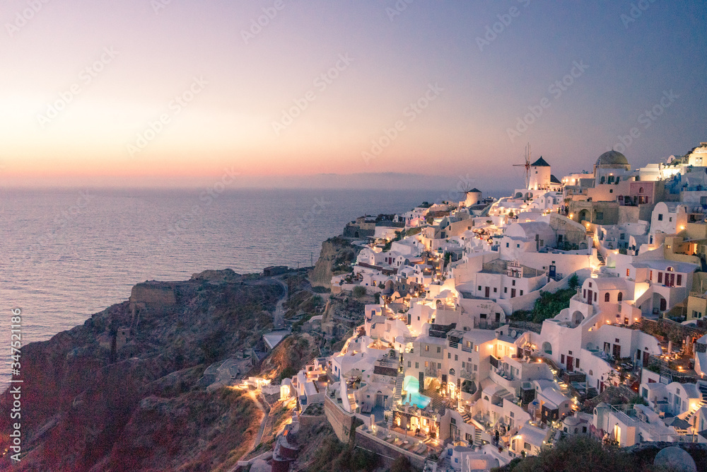 View of Oia and windmill from castle ruins at sunset, Santorini island, Cyclades, Greece